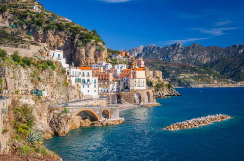 Italian coastal town with white buildings and orange roofs on steep cliffs above deep blue water.